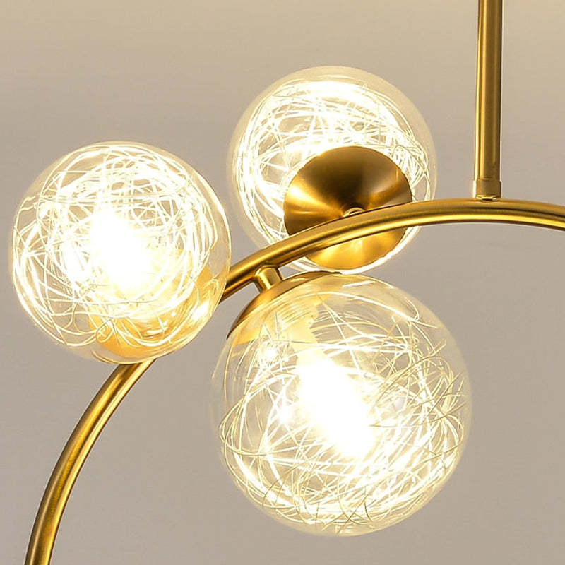 Close-up of the Clérachic brass ring globe pendant's clear glass globes, showing the fine gold wire nest glowing around the LED bulb.