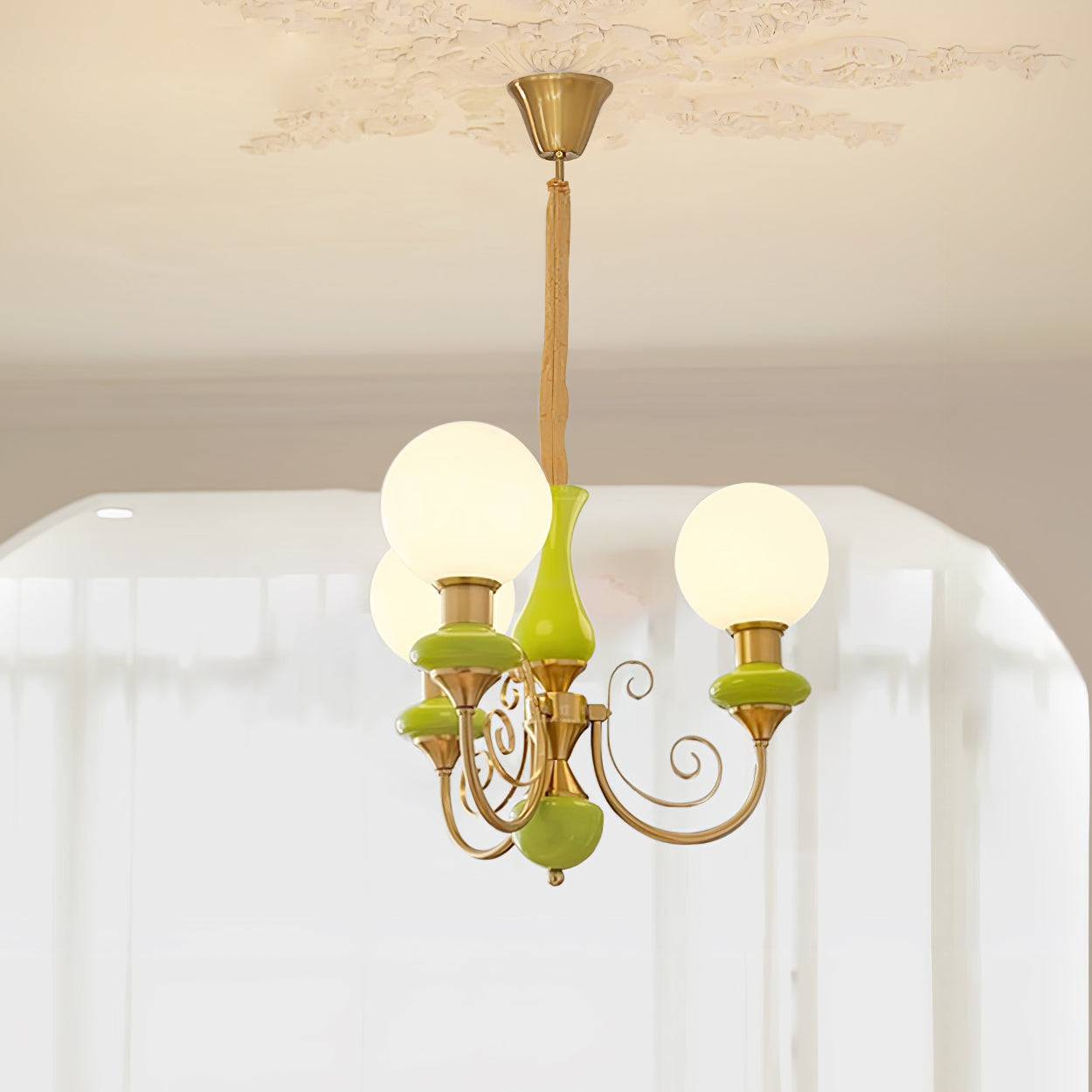 Clérachic Brass Scrollwork Chandelier in green, three lit opal globes on curved brass arms below an ornate ceiling rose.