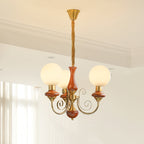 Red-brown Clérachic Brass Scrollwork Chandelier with three opal globes lit against a white corniced ceiling.