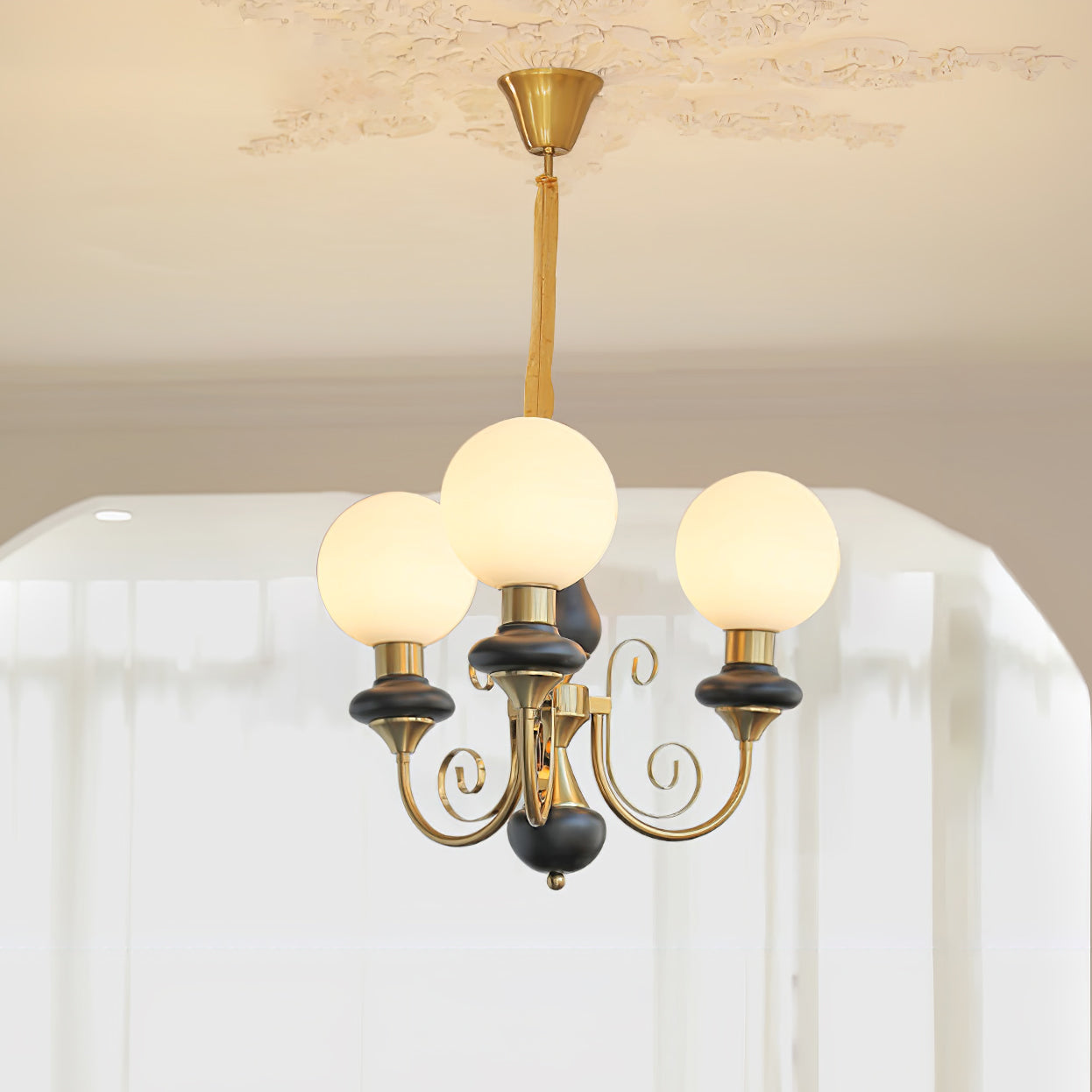 Black-stemmed Clérachic Brass Scrollwork Chandelier with three opal globes glowing under a plaster ceiling medallion.