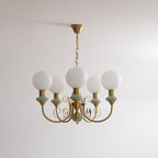 Clérachic Brass Scrollwork Chandelier in soft sage green, five lights hung unlit on a brass chain against a plain wall.