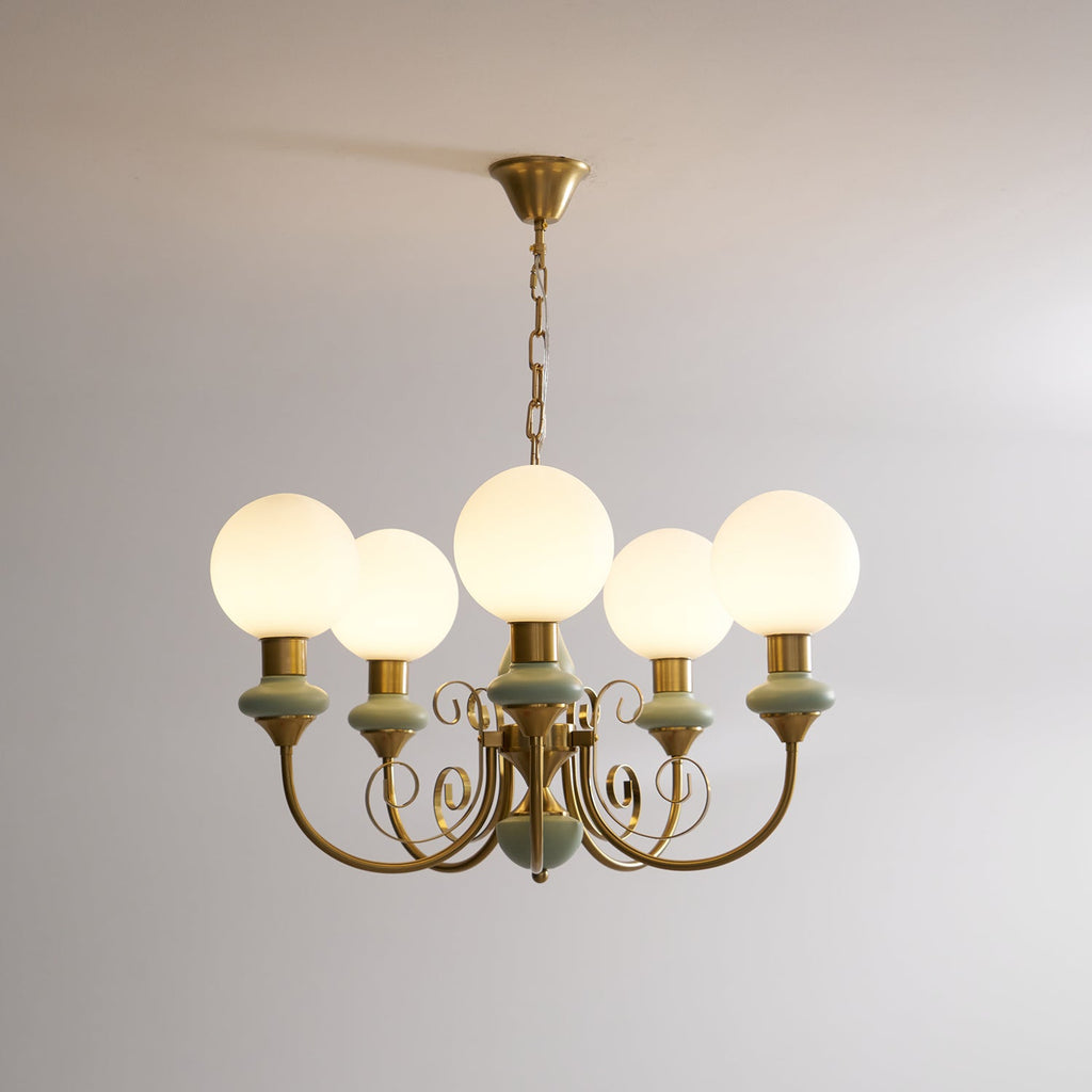 Sage-green Clérachic Brass Scrollwork Chandelier lit on its brass chain, opal globes glowing against a bare wall.