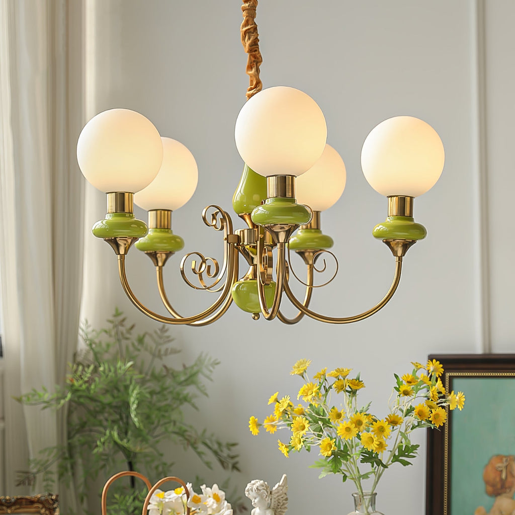 Clérachic Brass Scrollwork Chandelier in green seen close, five lit globes above a table of yellow daisies and greenery.