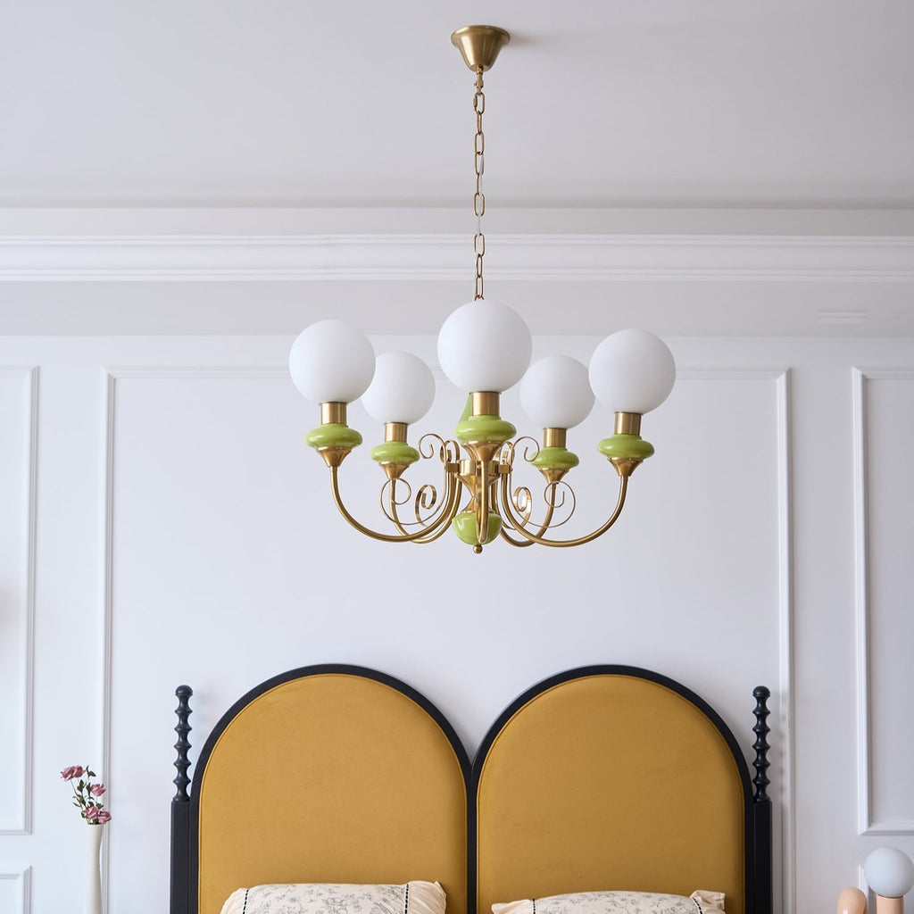 Five-light Clérachic Brass Scrollwork Chandelier on a brass chain above a mustard arched headboard in a panelled bedroom.
