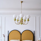 Five-light Clérachic Brass Scrollwork Chandelier on a brass chain above a mustard arched headboard in a panelled bedroom.