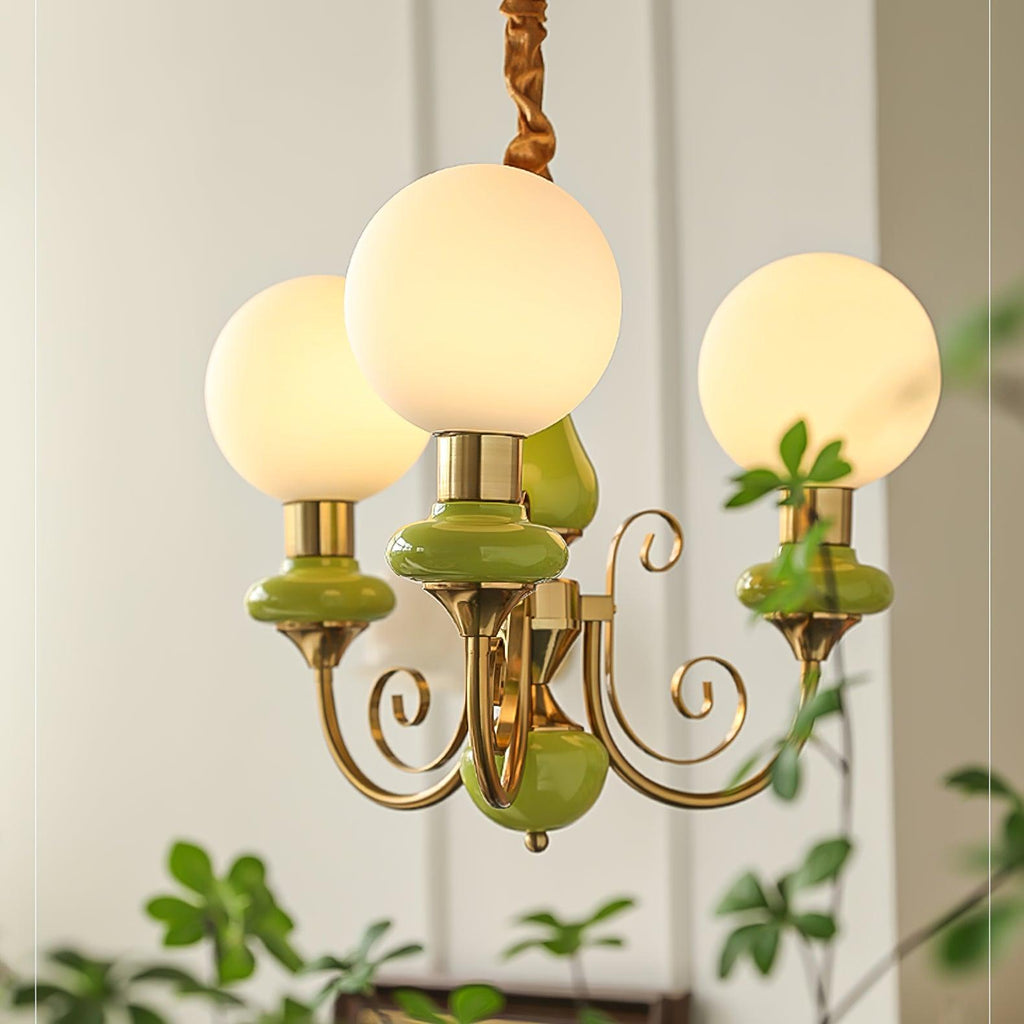 Clérachic Brass Scrollwork Chandelier in green shown close, three globes lit against a panelled wall with trailing ivy.