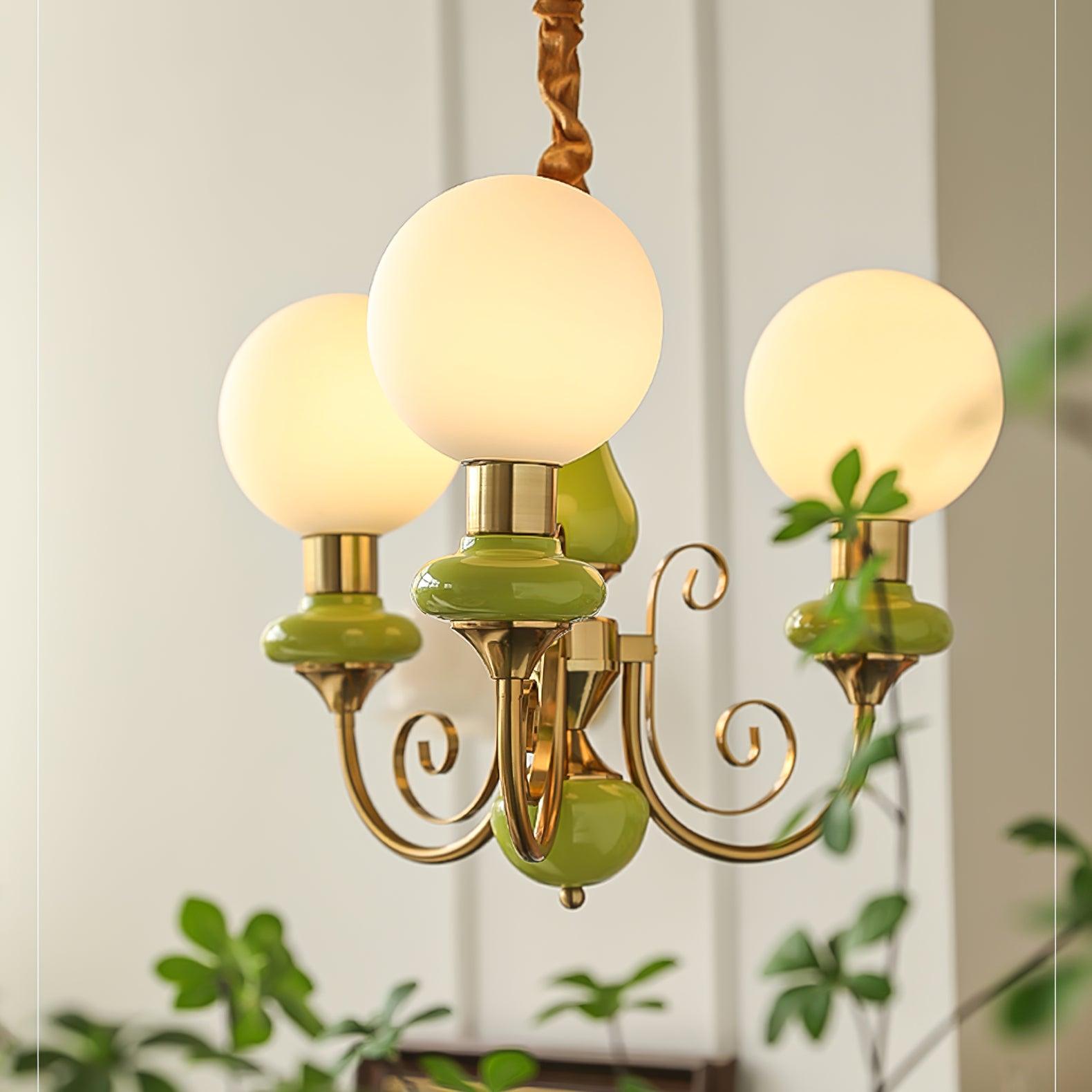 Clérachic Brass Scrollwork Chandelier in green shown close, three globes lit against a panelled wall with trailing ivy.