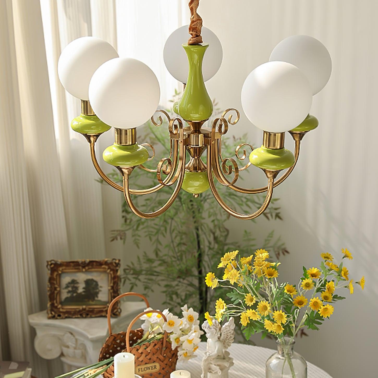 Green Clérachic Brass Scrollwork Chandelier lit in a styled room with a gilt landscape, wicker basket and daisies.