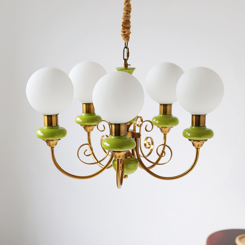 Clérachic Brass Scrollwork Chandelier in green on a short brass chain and hook, five opal globes against a plain wall.