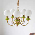 Clérachic Brass Scrollwork Chandelier in green on a short brass chain and hook, five opal globes against a plain wall.