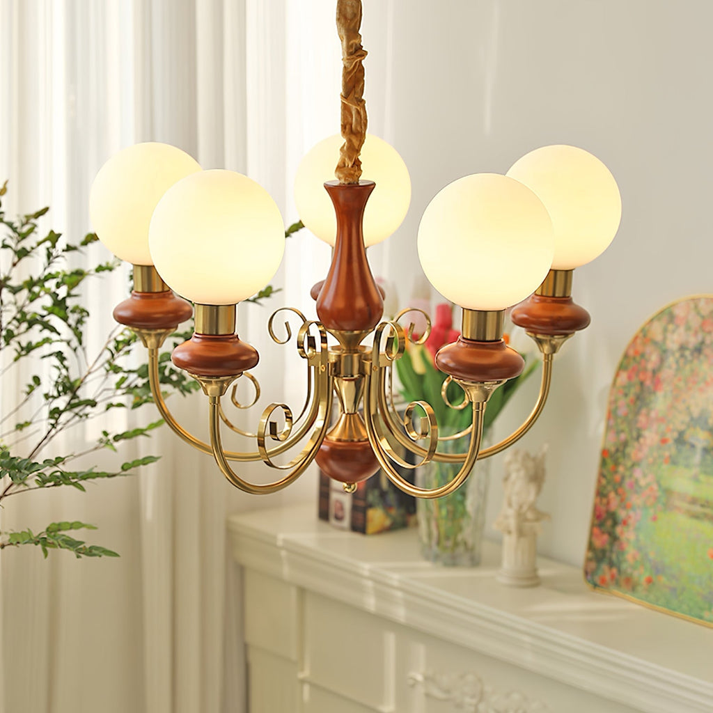 Red-brown Clérachic Brass Scrollwork Chandelier lit beside a mantel set with tulips and a framed garden painting.
