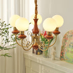 Red-brown Clérachic Brass Scrollwork Chandelier lit beside a mantel set with tulips and a framed garden painting.