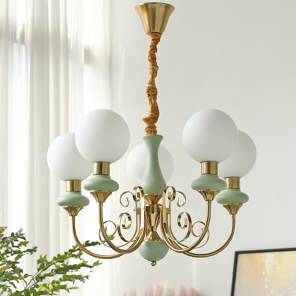 Sage-green Clérachic Brass Scrollwork Chandelier lit on a long fabric flex in front of bright window sheers.
