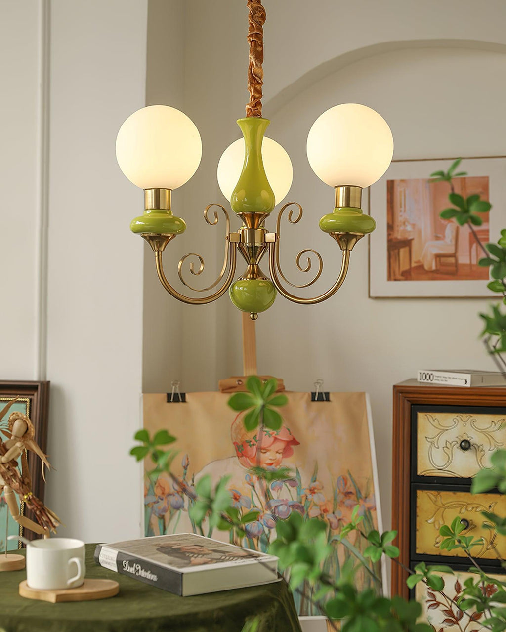 Green three-light Clérachic Brass Scrollwork Chandelier lit in an arched alcove above an easel and a painted canvas.