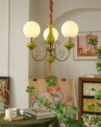 Green three-light Clérachic Brass Scrollwork Chandelier lit in an arched alcove above an easel and a painted canvas.