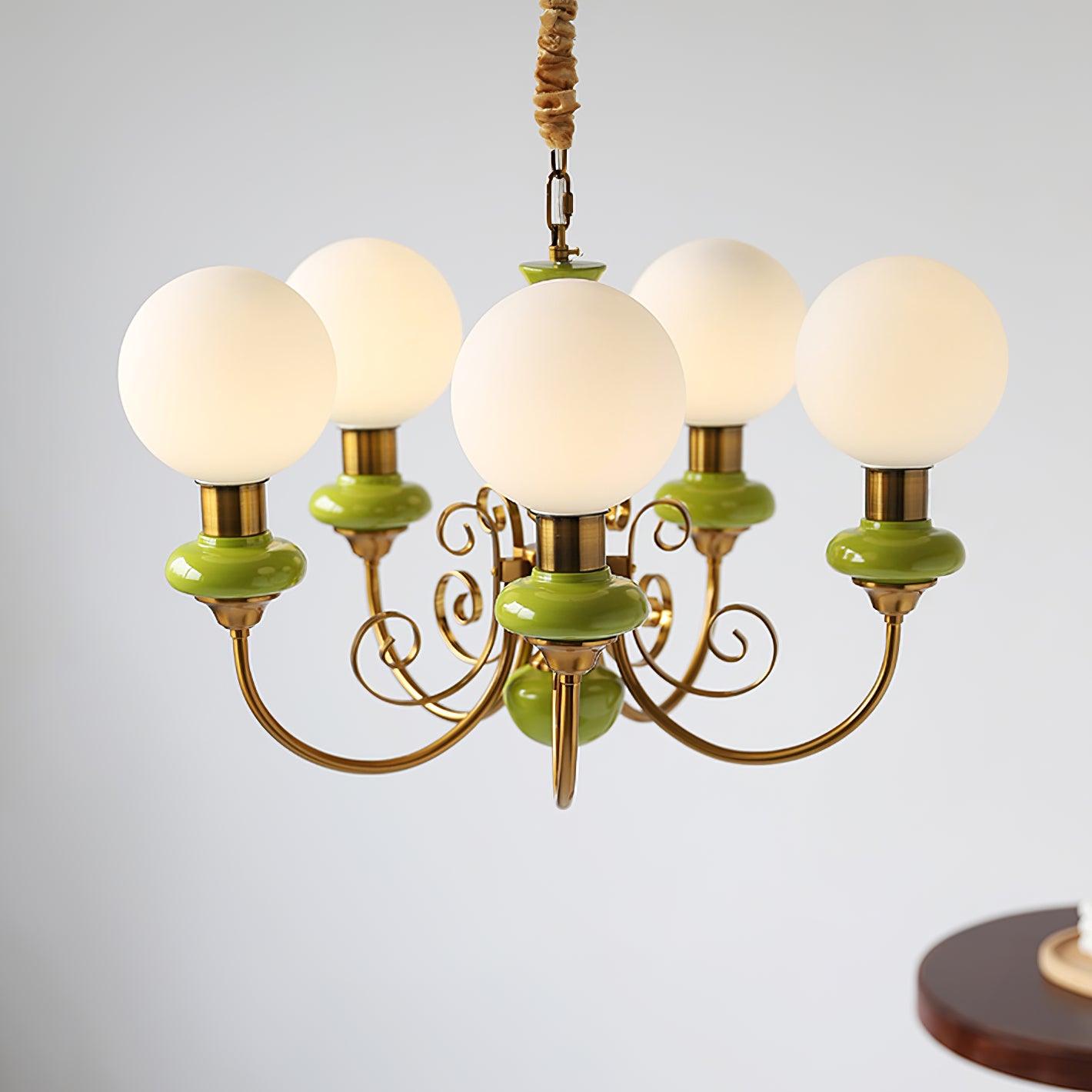 Clérachic Brass Scrollwork Chandelier in green on a brass chain, five opal globes lit against a plain grey wall.