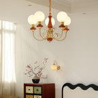 Red-brown Clérachic Brass Scrollwork Chandelier lit in a room with a painted cabinet and a matching wall light.