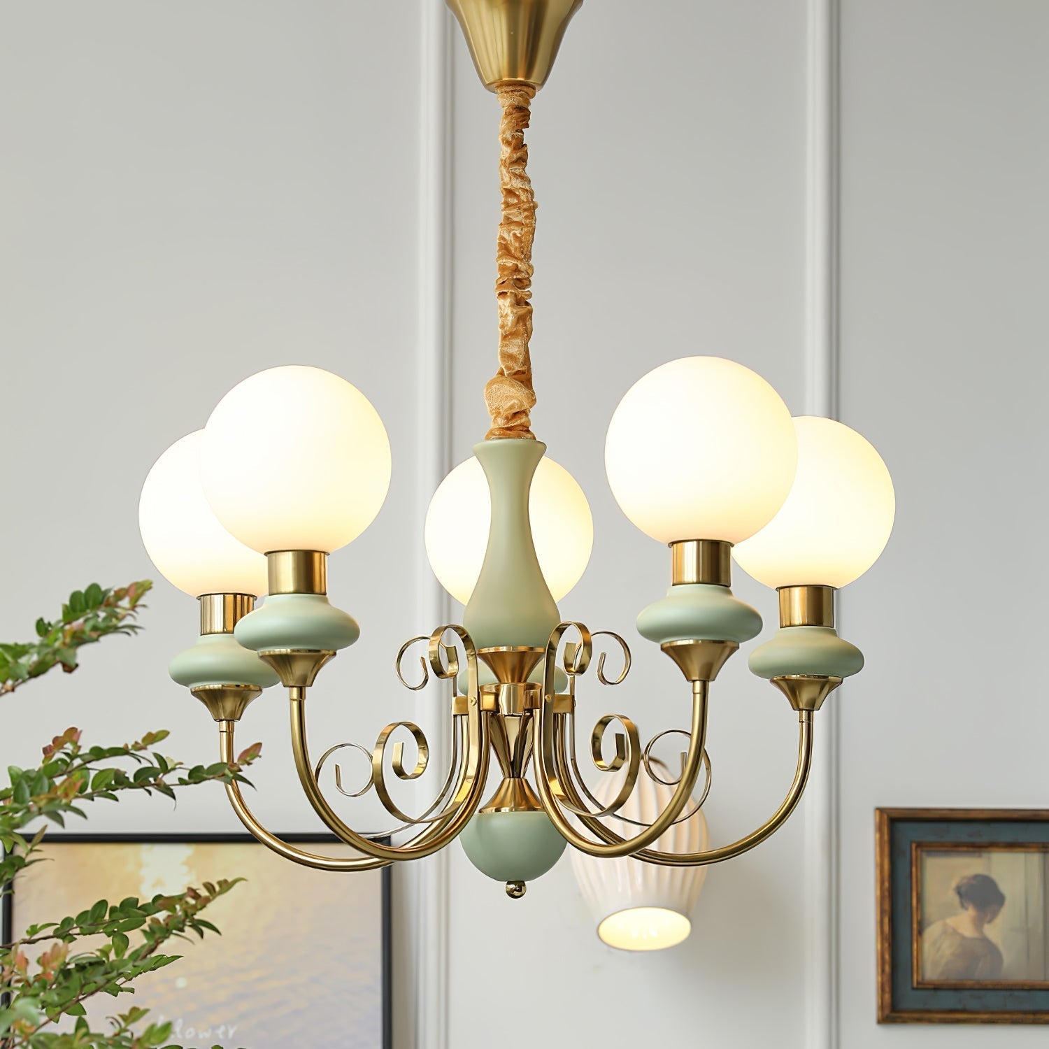 Clérachic Brass Scrollwork Chandelier in sage green, five lights lit beside a framed portrait on a panelled wall.