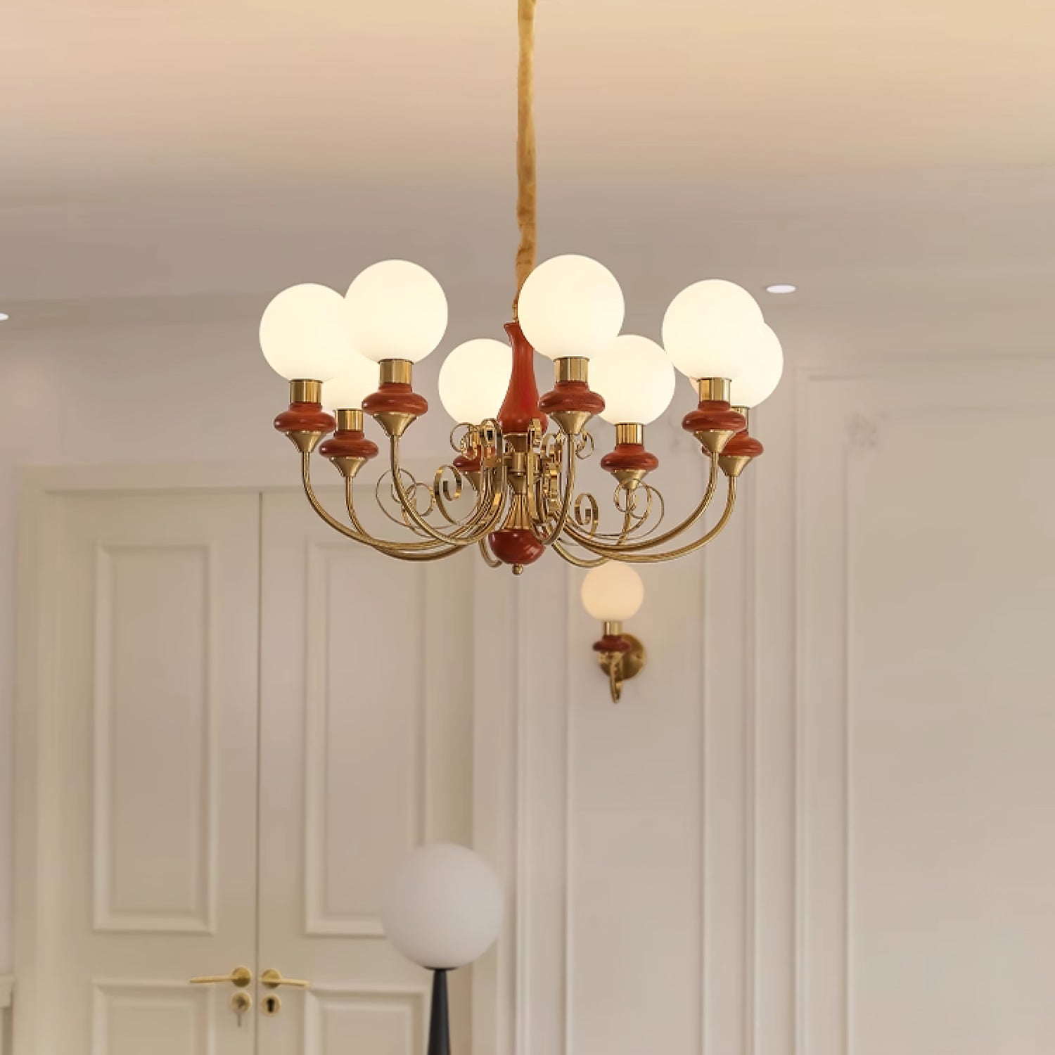 Eight-light Clérachic Brass Scrollwork Chandelier in red-brown, lit above panelled doors beside the matching sconce.