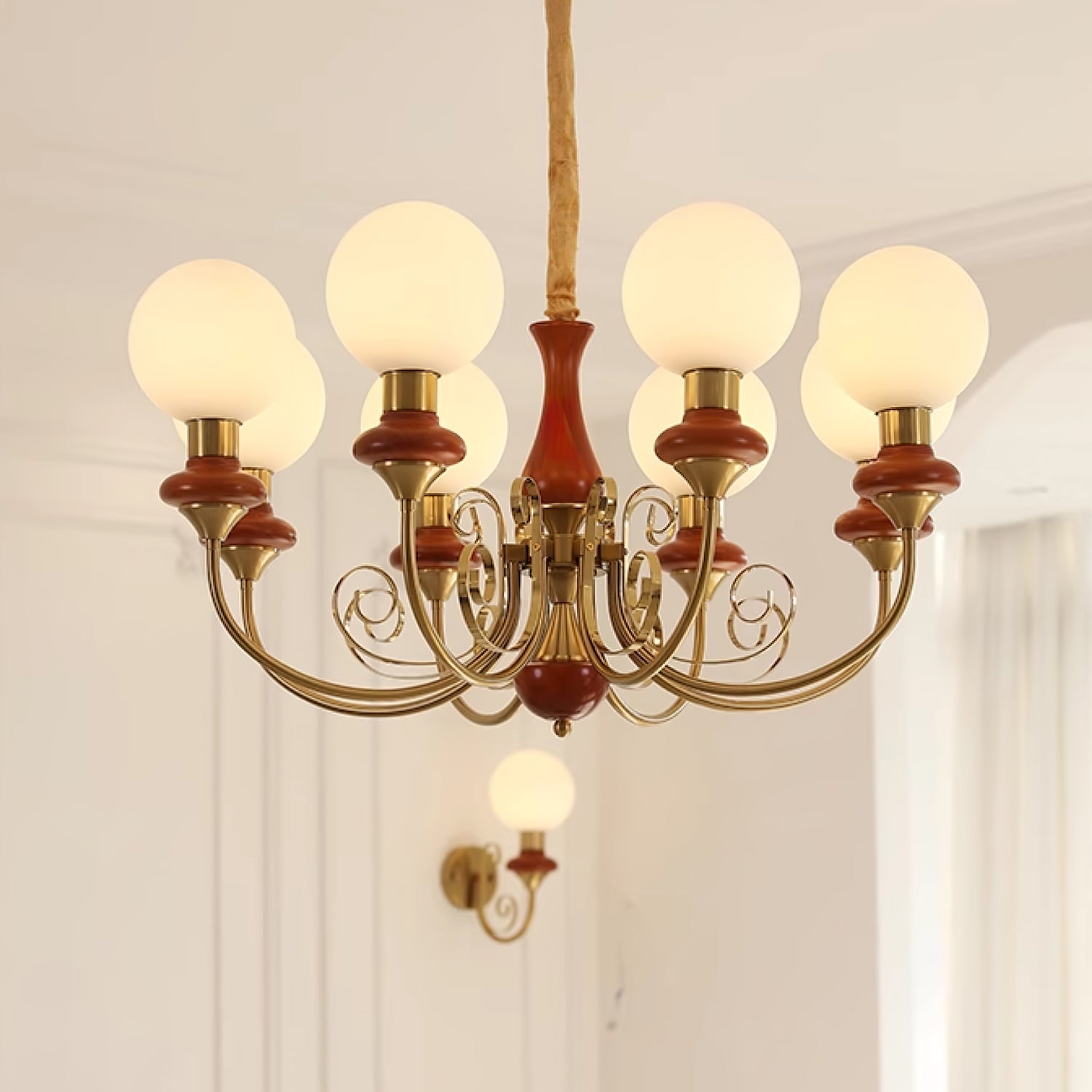 Red-brown Clérachic Brass Scrollwork Chandelier with eight lit globes, its glossy turned collars catching the light.