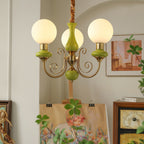 Clérachic Brass Scrollwork Chandelier in green, three lit globes above an easel in a softly arched painting corner.