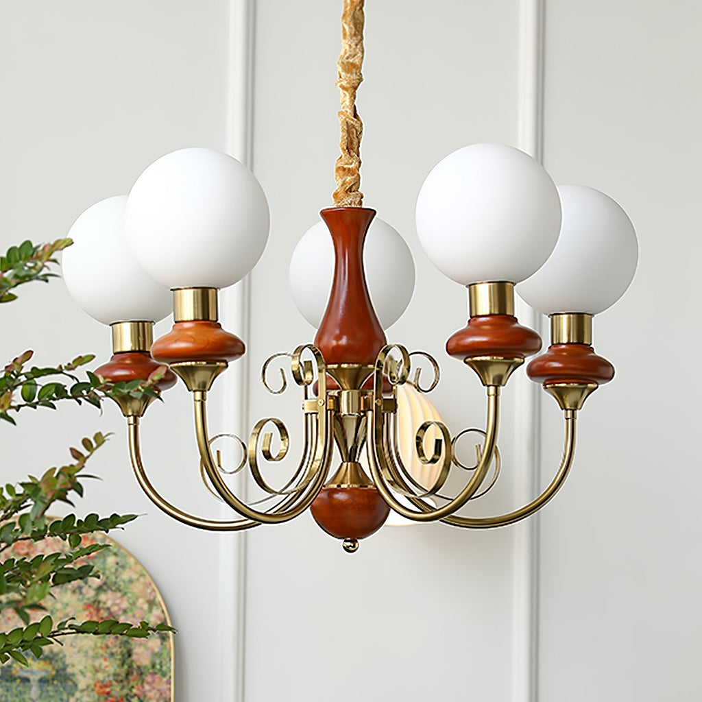 Red-brown Clérachic Brass Scrollwork Chandelier lit against a panelled wall, five opal globes and a mirror behind.