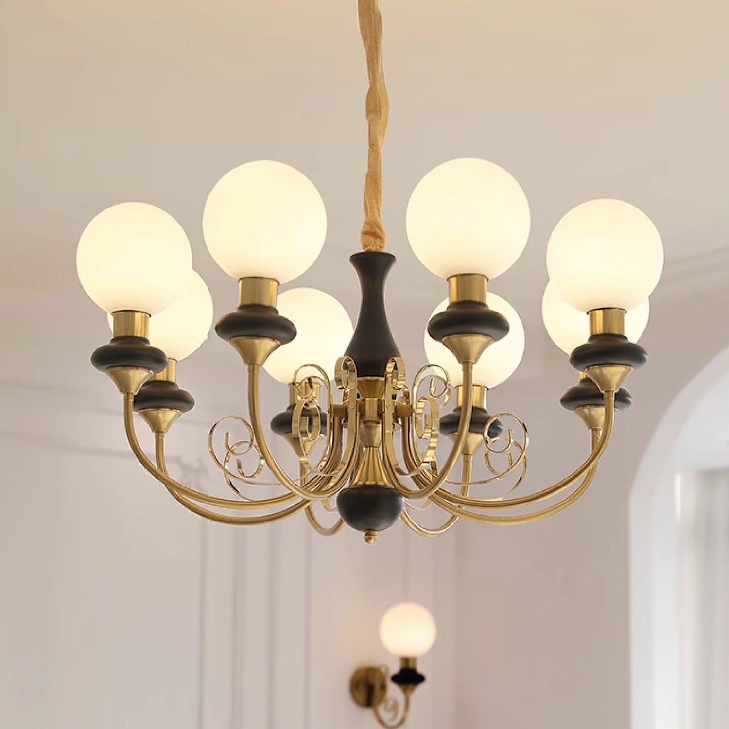 Clérachic Brass Scrollwork Chandelier in black, eight globes lit above a panelled wall with the matching sconce below.