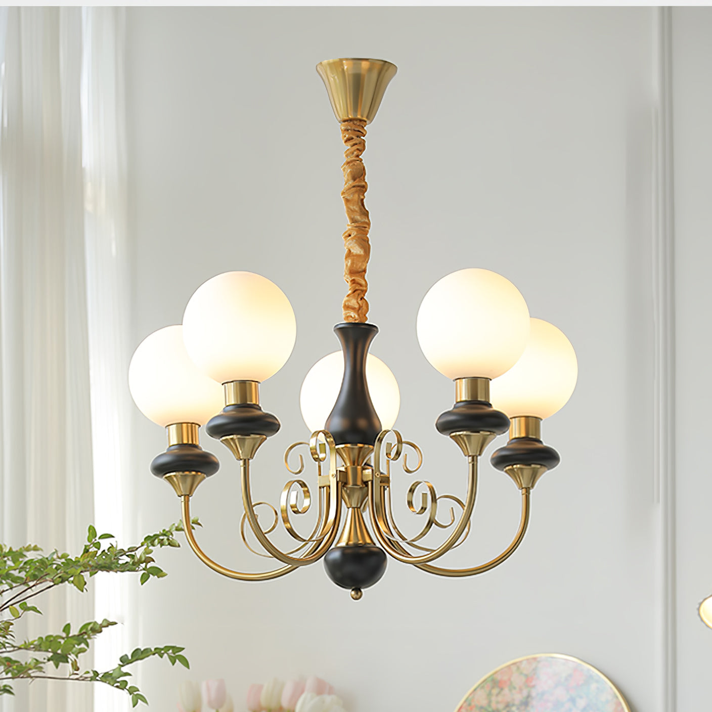 Black-stemmed Clérachic Brass Scrollwork Chandelier, five lit globes in front of bright sheer curtains and tulips.