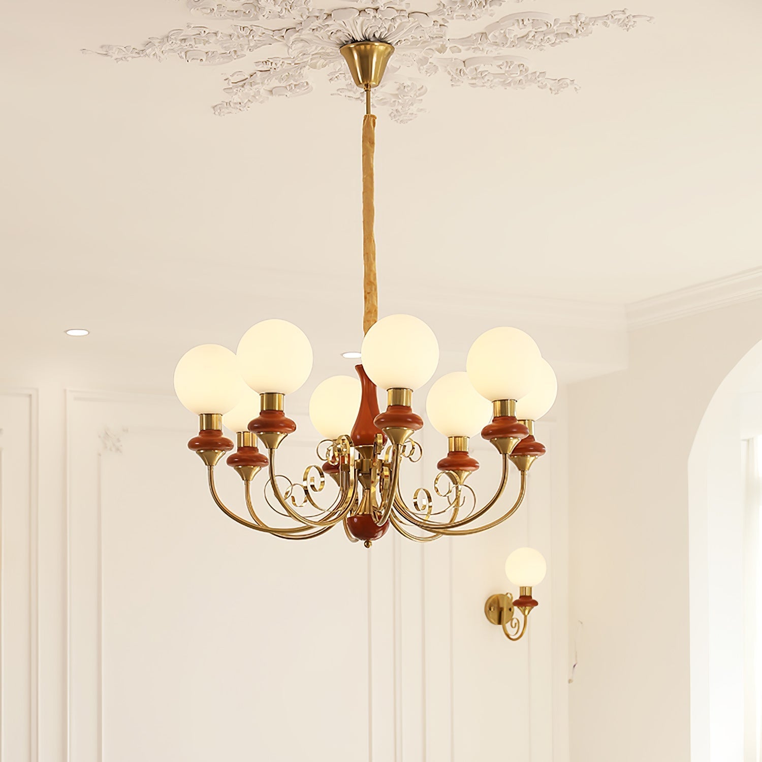 Red-brown Clérachic Brass Scrollwork Chandelier with eight lights, hung from a plaster rose beside a matching sconce.