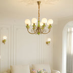Green Clérachic Brass Scrollwork Chandelier in the eight-light size, lit above a panelled living room and pale sofa.
