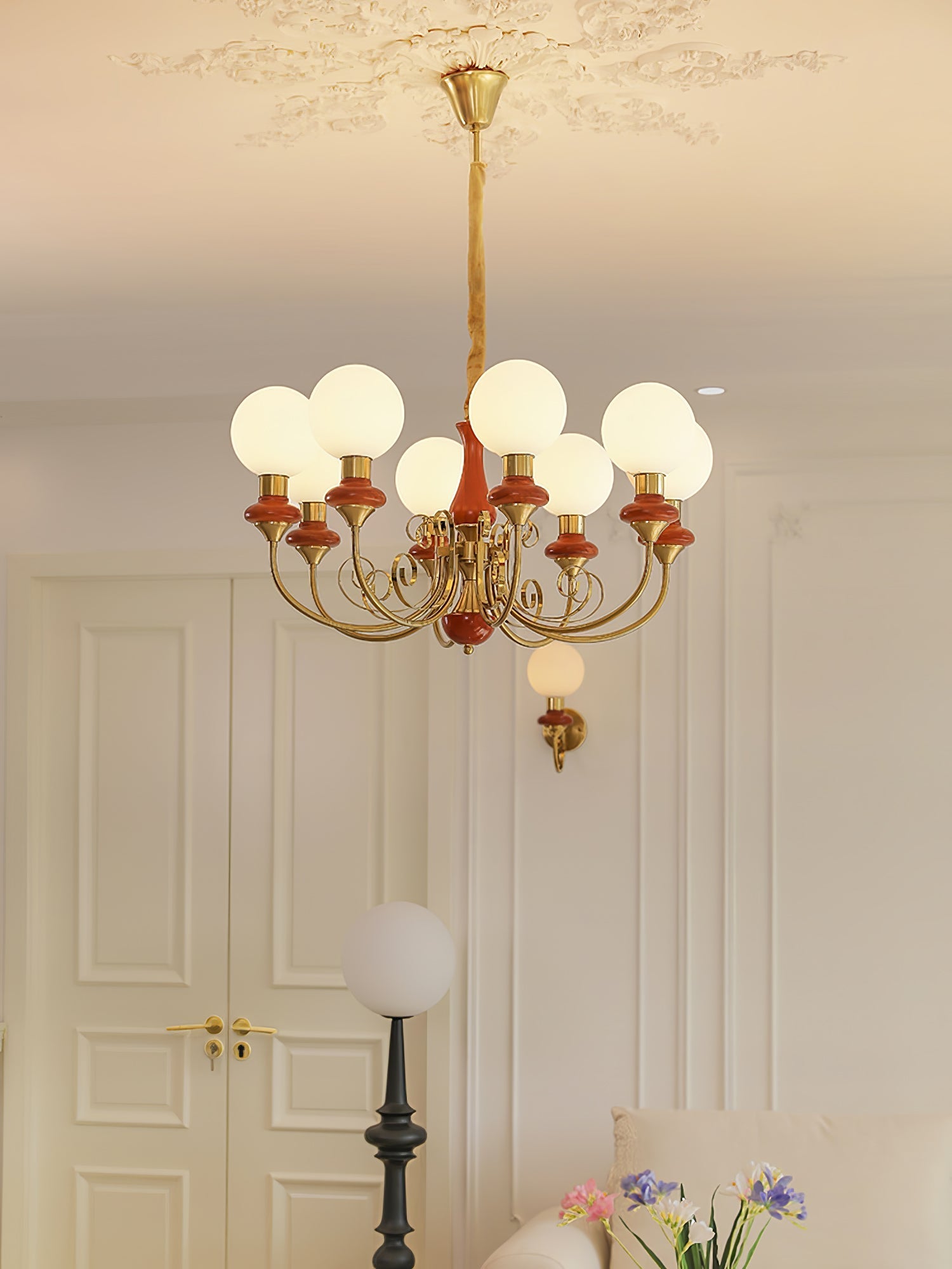 Eight-light Clérachic Brass Scrollwork Chandelier in red-brown, lit near tall panelled doors and a globe floor lamp.