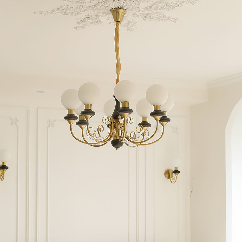 Black Clérachic Brass Scrollwork Chandelier with eight globes lit above a panelled wall flanked by matching sconces.