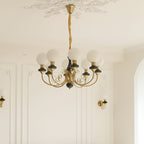 Black Clérachic Brass Scrollwork Chandelier with eight globes lit above a panelled wall flanked by matching sconces.