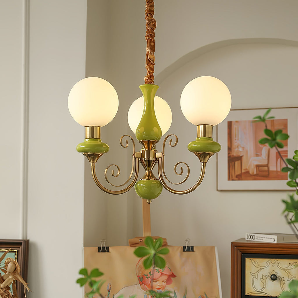 Clérachic Brass Scrollwork Chandelier in green, three lit globes in an arched studio corner above a canvas on an easel.