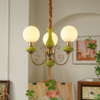 Clérachic Brass Scrollwork Chandelier in green, three lit globes in an arched studio corner above a canvas on an easel.
