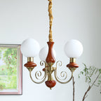 Three-light Clérachic Brass Scrollwork Chandelier in red-brown, lit beside a window looking onto a flowering garden.
