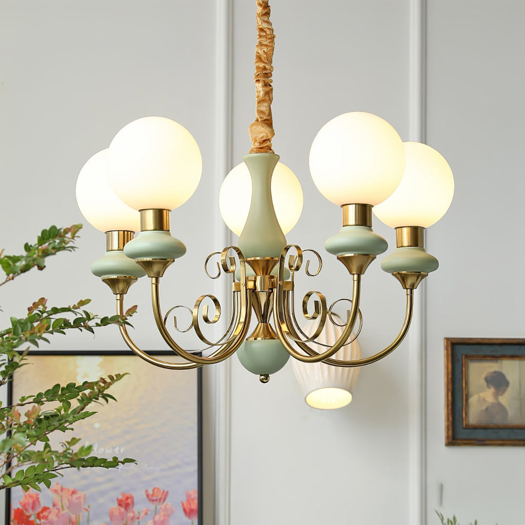 Clérachic Brass Scrollwork Chandelier in sage green, five lit globes beside a framed print and a ribbed wall light.