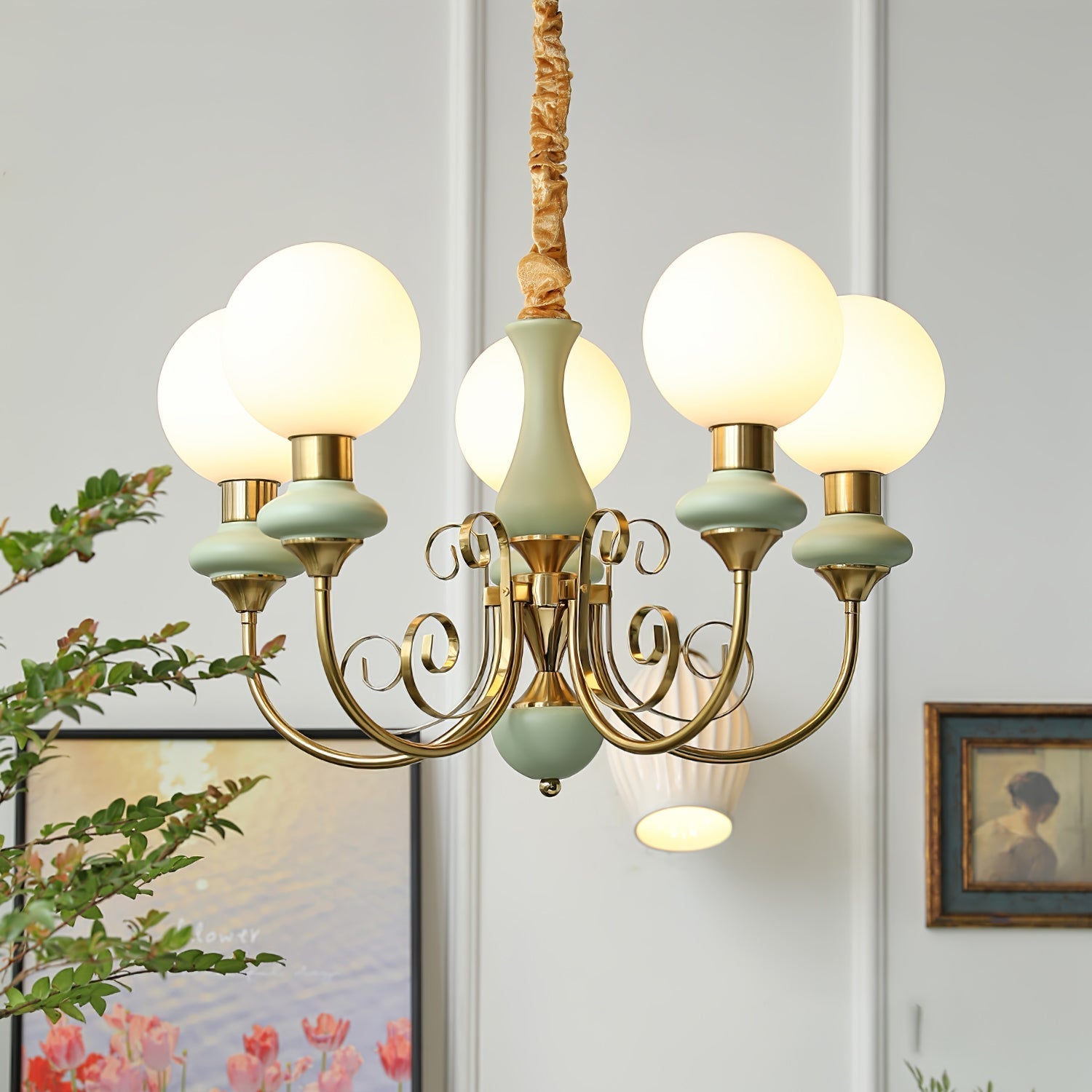 Clérachic Brass Scrollwork Chandelier in sage green, five lit globes beside a framed print and a ribbed wall light.