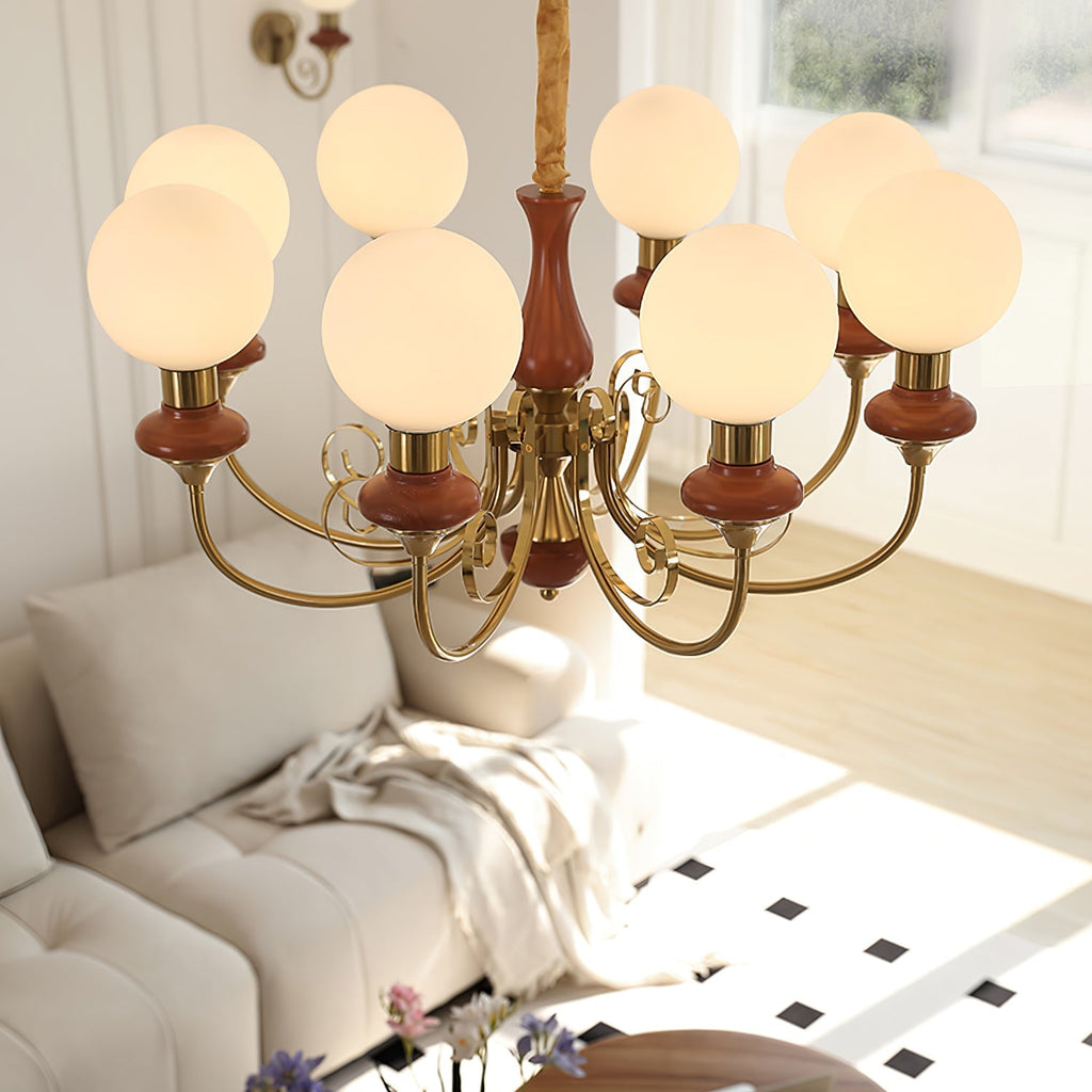 Clérachic Brass Scrollwork Chandelier in red-brown seen from above, eight lit globes over a pale sofa and tiled floor.