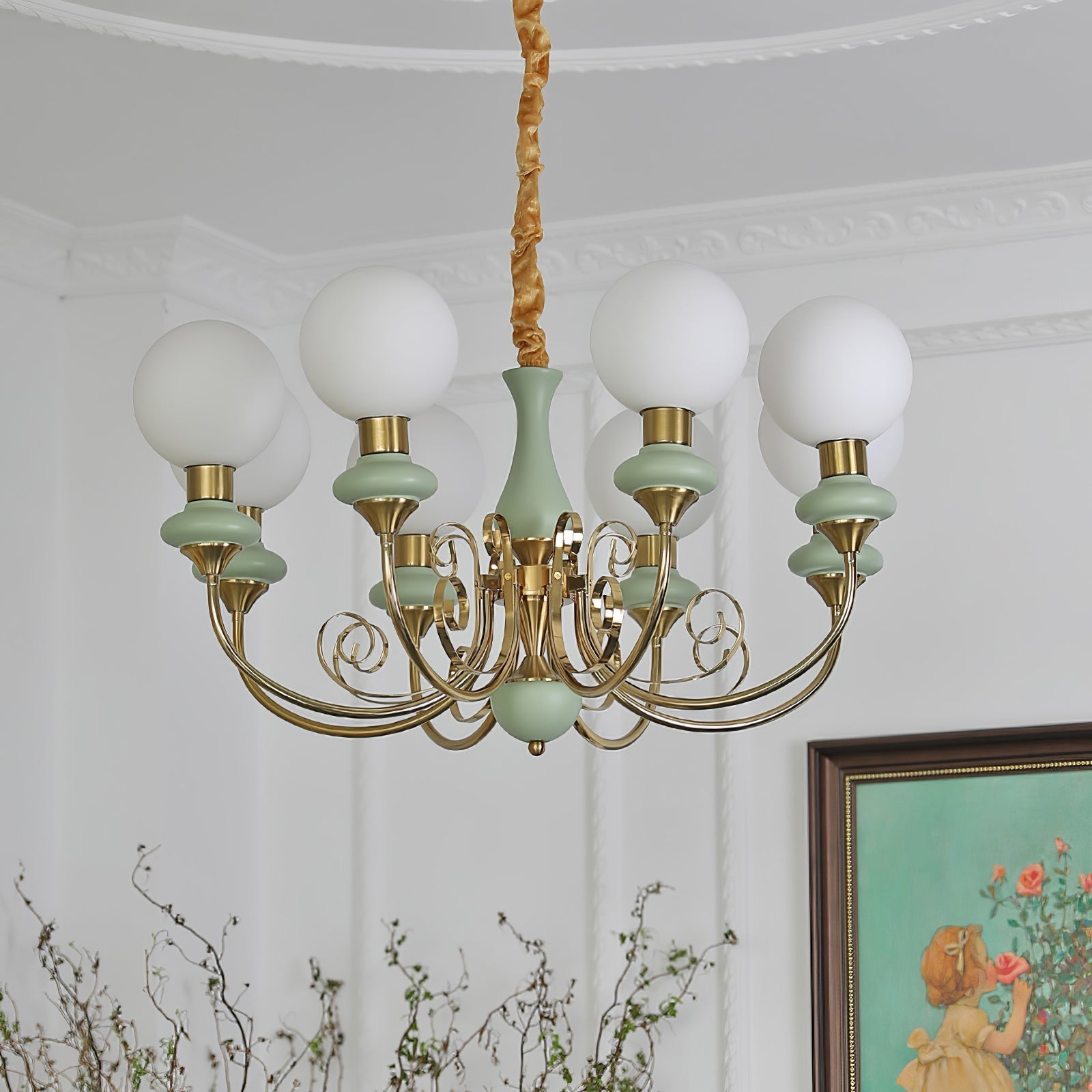 Sage-green Clérachic Brass Scrollwork Chandelier with eight lit globes, a framed rose painting on the wall behind.