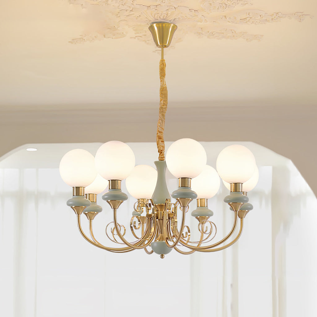 Clérachic Brass Scrollwork Chandelier in sage green, eight lit globes hung from a moulded rose above sheer curtains.