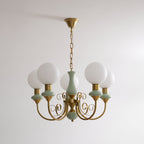 Sage-green Clérachic Brass Scrollwork Chandelier shown unlit on a brass chain against a plain white studio wall.
