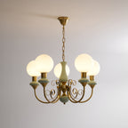 Clérachic Brass Scrollwork Chandelier in sage green on a brass chain, five opal globes lit against a bare wall.