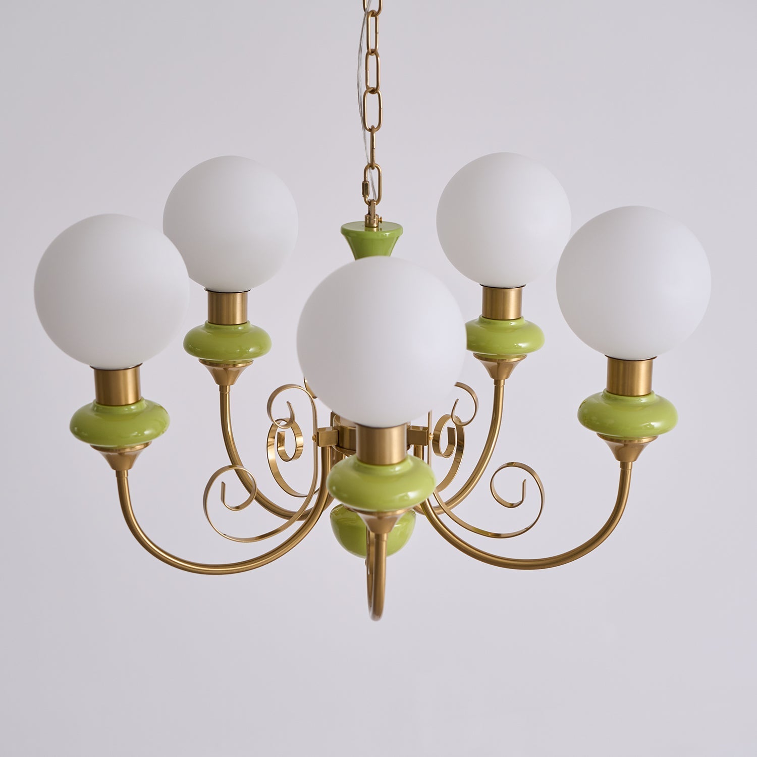 Green Clérachic Brass Scrollwork Chandelier seen close and lit, five opal globes above the curled brass volutes.
