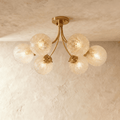 Clérachic six-head semi-flush ceiling light with curved brass arms and ribbed glass globes, lit warm against a limewash ceiling.