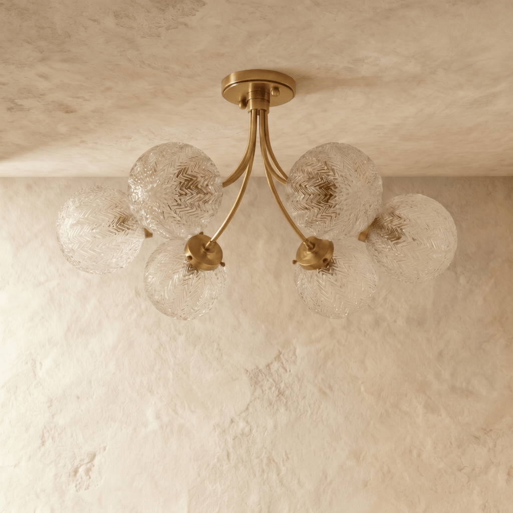 Clérachic six-head brass ceiling light with curved arms and clear herringbone-textured glass globes, unlit on a limewash ceiling.