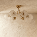 Clérachic six-head brass ceiling light with curved arms and clear herringbone-textured glass globes, unlit on a limewash ceiling.