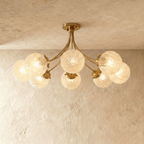Clérachic eight-head semi-flush ceiling light with sweeping brass arms and ribbed glass globes on a limewash ceiling.