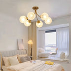 Clérachic six-head brass ceiling light with frosted textured globes above a bed, beside a bay window with sheer curtains.