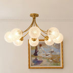 Clérachic eight-head brass ceiling light with ribbed glass globes lit warm, below a cornice and a gilt-framed painting.